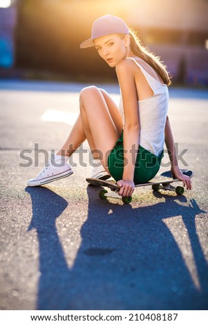 Closeup summer portrait of pretty young woman posing in urban, hipster girl with skate board in town. Summer evening sunlight