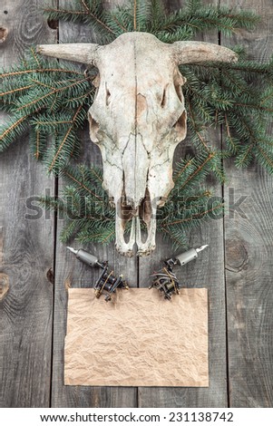 Pine branch with skull and tattoo machine liner and shader on wooden background. Copy space