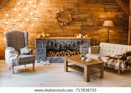 Home comfort. Armchair near the fireplace with firewood. Photo of interior of room with a wooden wall, wreath and garlands, Christmas atmosphere