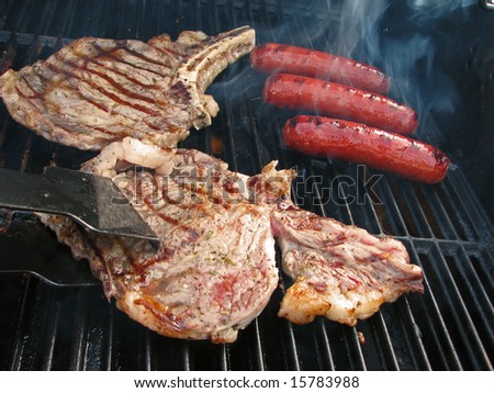 Turning a steak while cooking on outdoor grill with bratwurst.