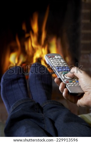 Man With Remote Control Watching Television And Relaxing By Fire