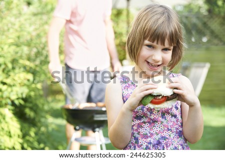 Young Girl Eating Beefburger At Family Barbecue
