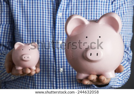 Man Holding Large And Small Piggy Bank
