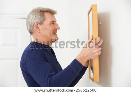 Mature Man Hanging Picture On Wall