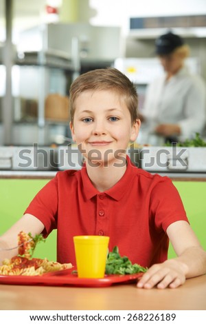 Male Pupil Sitting At Table In School Cafeteria Eating Lunch