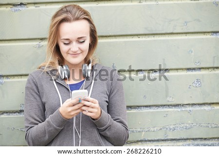 Teenage Girl Wearing Headphones And Listening To Music In Urban