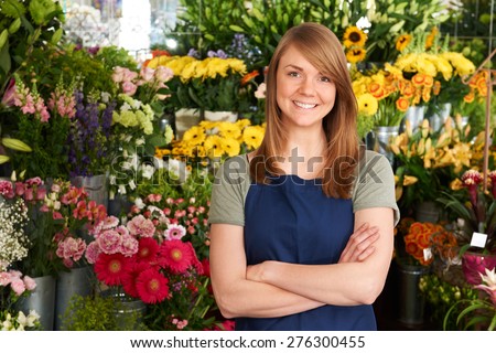 Florist Standing In Shop In Front Of Flower Display