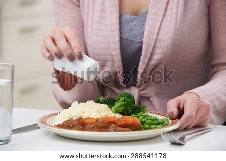 Woman At Home Adding Salt To Meal