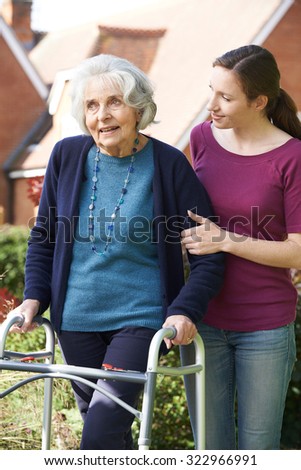 Daughter Helping Senior Mother To Use Walking Frame