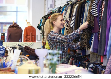 Female Shopper In Thrift Store Looking At Clothes