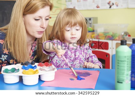 Teacher Helping Pre School Child In Art Class