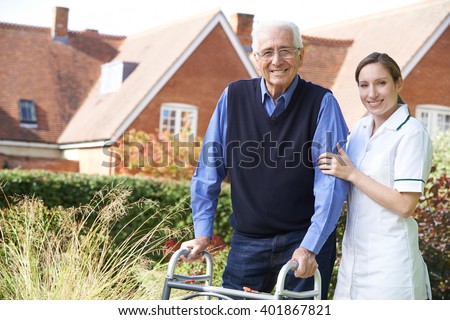 Care giver Helping Senior Man To Walk In Garden Using Walking Frame
