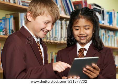 Pupils Wearing School Uniform Using Digital Tablet In Library