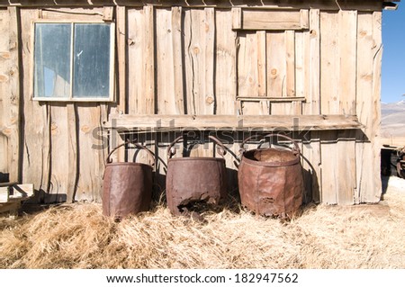 Three iron barrels resting against the side of an old wooden house.