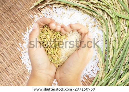 White and brown rice held in heart shaped hand over white rice background.