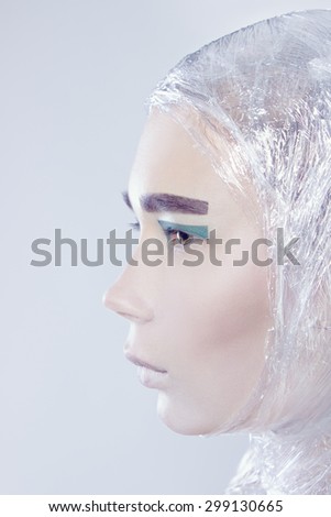Profile of misterous pretty woman wrapped in cellophane looking forward standing on light grey background, vertical picture