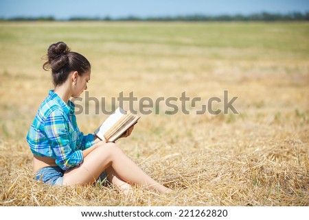young girl sitting on golden reap wheat in yellow sunset field Woman holding in hands interesting book, reading text