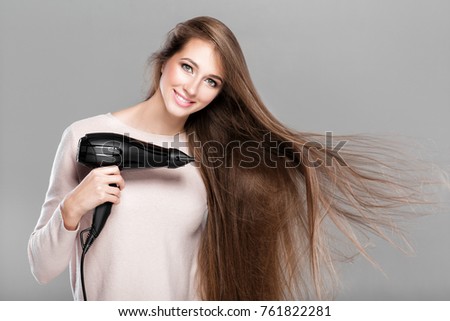 portrait of beautiful smiling woman drying her long hair with dryer over gray background