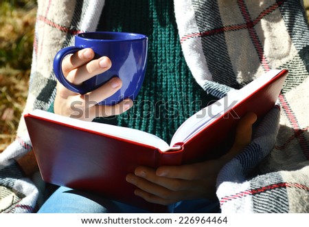 a young girl wrapped in a warm plaid, reading a book in the Park.hot drinks, warming, herbal tea.Autumn concept