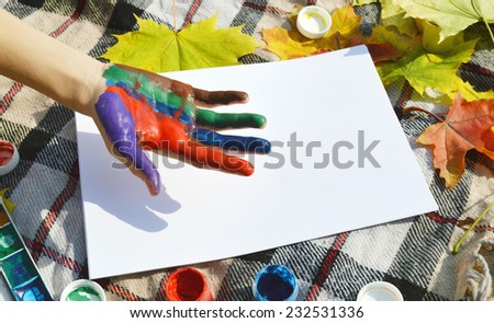 a young,beautiful girl draws a hand print on the paper paints