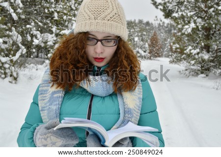 beautiful,young,curly girl,dressed in a jacket, knitted hat, knitted scarf,reads thoughtfully book in the Park