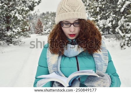 beautiful,young,curly girl,dressed in a jacket, knitted hat, knitted scarf,reads thoughtfully book in the Park