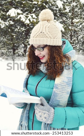 young,beautiful,curly,dark-haired girl dressed in a turquoise jacket,bodily woolly hat, and a light blue scarf,reading a book in the Park,drinking tea,coffee,cocoa