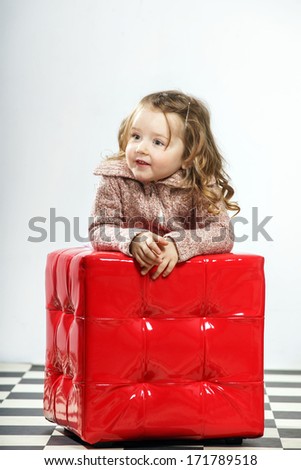 Cute little girl with red cube-chair posing in studio