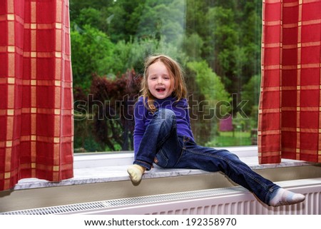 Cute little girl playing with drapes on the window marble  sill