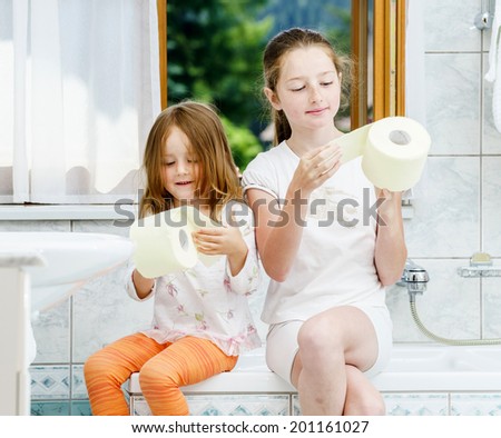 Two sisters playing with toilet paper roll in bathroom