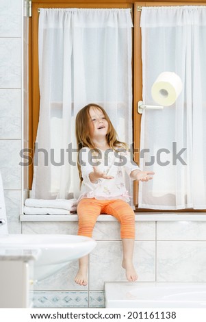 Cute little girl playing with toilet paper roll in a bathroom