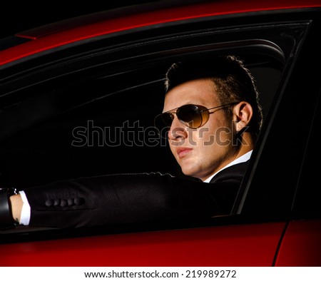Young elegant guy sitting in luxury  modern red car