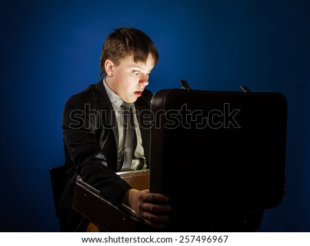 Affective teenage boy finding treasure in retro suitcase, isolated on blue
