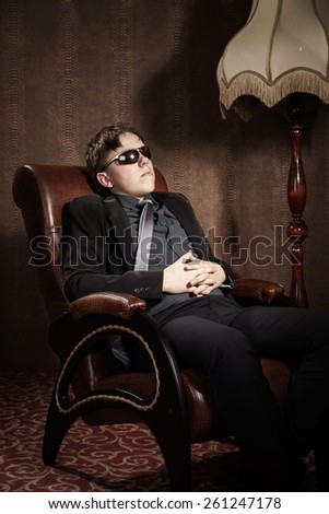 Elegant teenage boy sitting in arm-chair, studio portrait