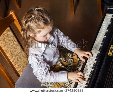 Cute little girl playing grand piano in music school, childhood concept