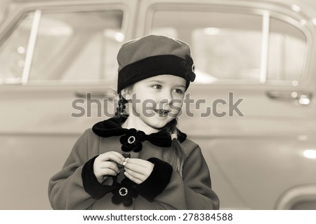 Cute little girl dressed in retro coat posing near oldtimer car, sixties