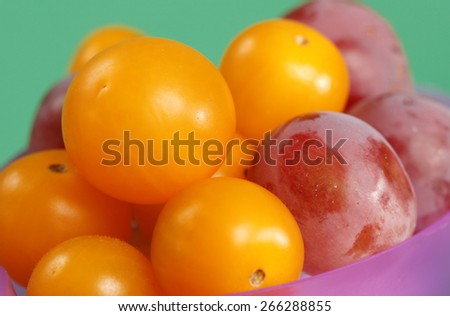Yellow Grape Tomatoes and Globe Grapes in a Purple Bowl on a Green Background