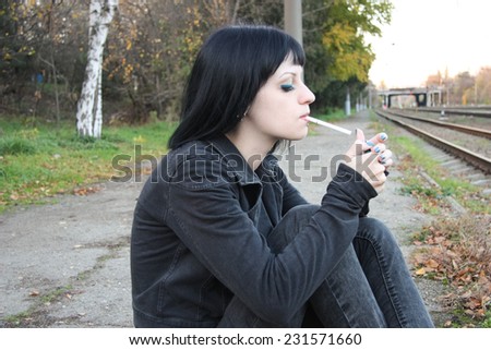 Girl smoke near rails and abandon railroad station