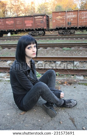 Girl sit between rails and abandon railroad station