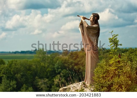 Girl in period costume playing the flute at the edge of the cliff.