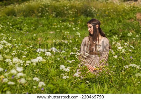 The girl in the image of an elf sitting in a meadow of grass and flowers