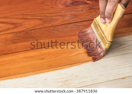 hand holding a brush applying varnish paint on a wooden surface