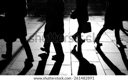 Dark silhouettes of the legs of four walking on the side walk in bright back light