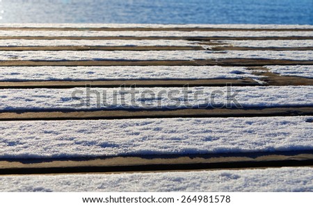 Low angle view of a bridge made of plank partly covered with snow and glimpse of the ocean
