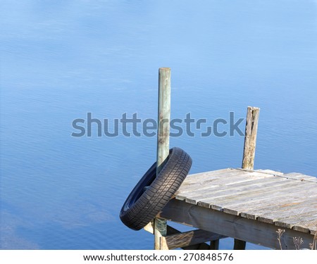 Silhouette of a tiny wooden bridge and a tyre. Calm blue water in the background