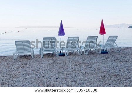 Five empty deck chair and parasol standing on the beach in the early morning before the tourists arrive