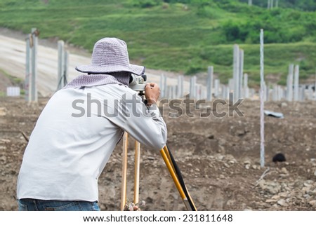 Builder surveyor working with optical equipment level at construction site.