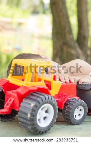 a little boy, two years old, smiling, summer, naked to the waist, sitting at a table playing with a red fire engine and a red tractor