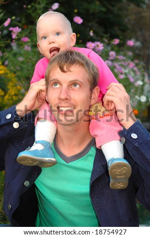 Proud father with his happy daughter sit on father\'s shoulders on flowers background.