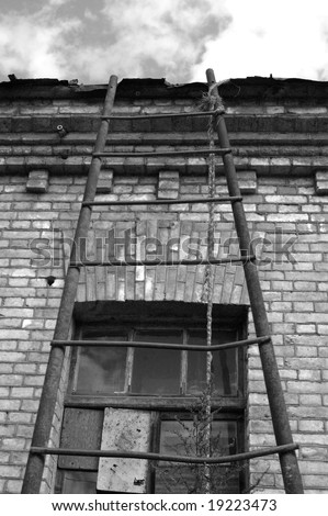 Rusty metal ladder lean on old building (brick wall with window) and cloud sky background - black-and-white image.